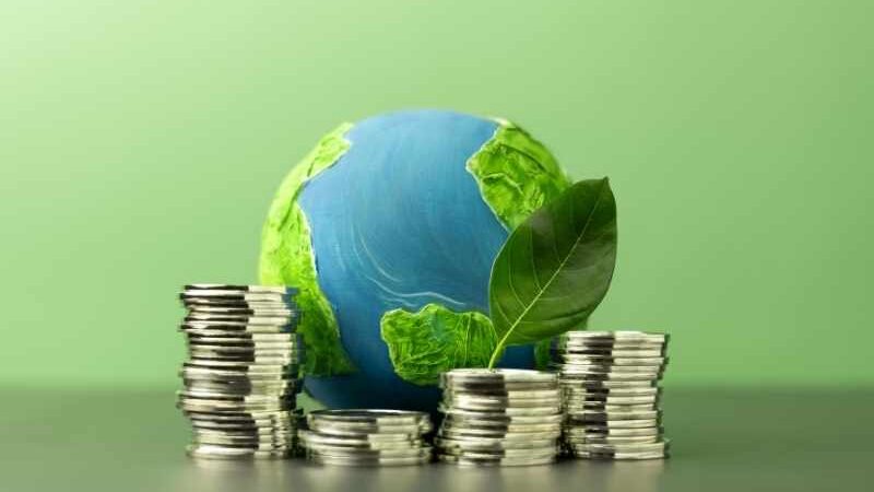 Se muestra el planeta tierra rodeado de vegetación y montones de monedas, representando la economía circular
