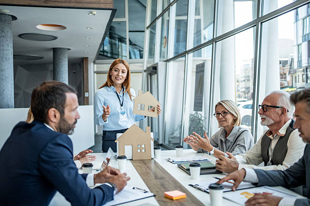 Agente inmobiliaria mostrando maquetas de viviendas a sus clientes durante una reunión en una oficina moderna, en la que se analizan opciones de inversión y compra de inmuebles